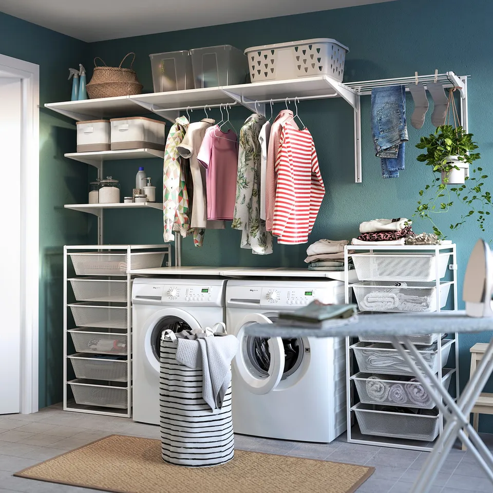 Organised laundry room with white JONAXEL storage shelves and mesh baskets, holding clothes and supplies.
