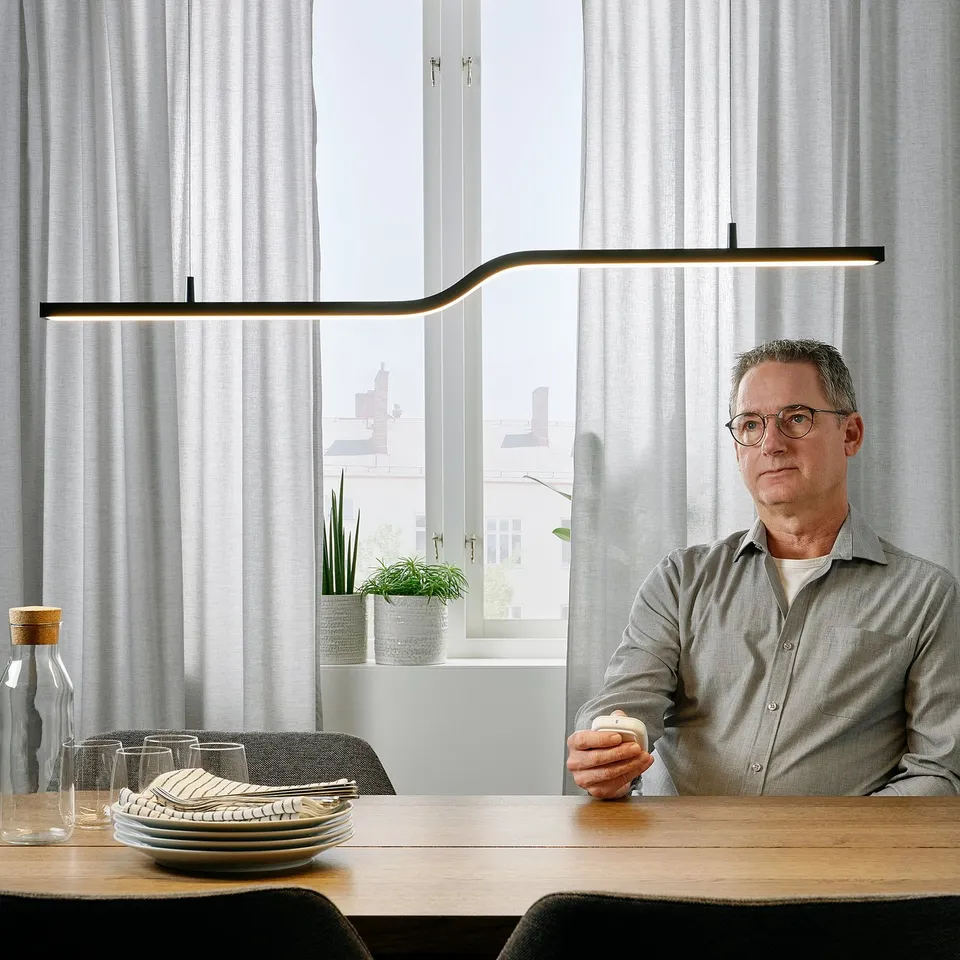 Person at table under PILSKOTT lamp with wireless dimming.