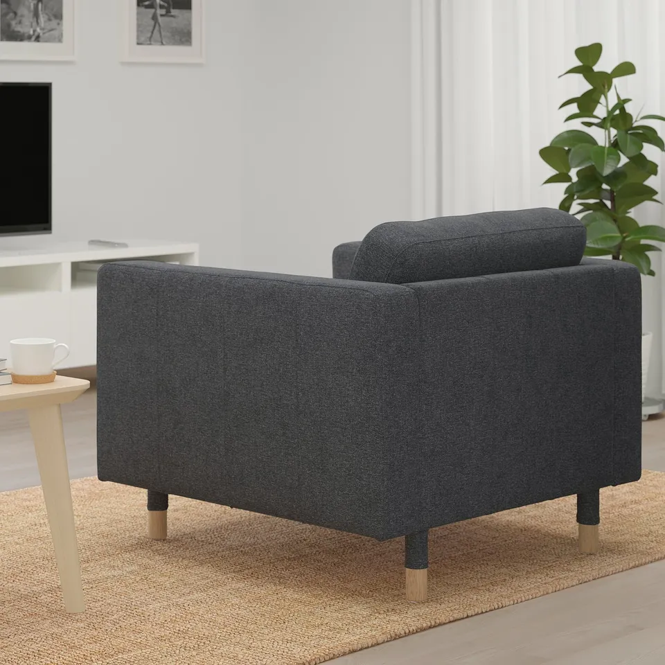 Dark grey upholstered armchair with wooden legs on a woven rug, beside a coffee table with mug.