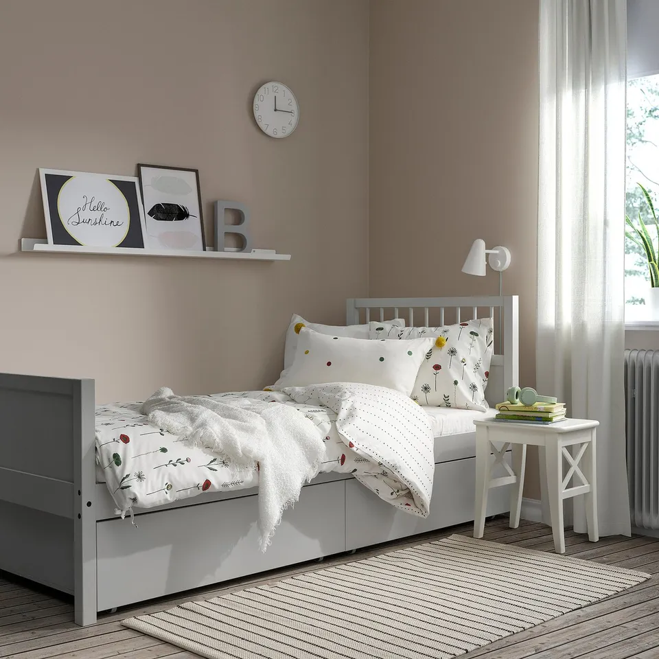 Cosy bedroom with a white SMYGA bed, featuring floral bedding and a grey side table.