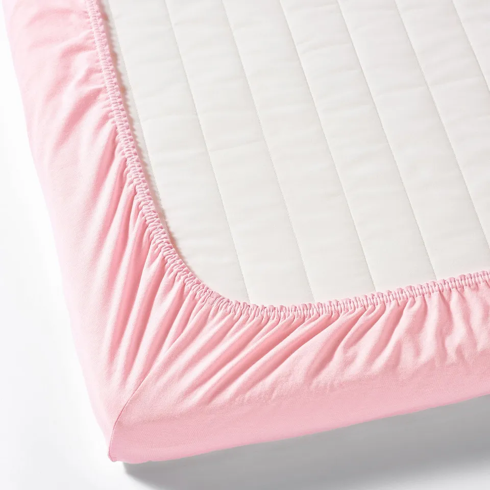 Pink fitted bed sheet with elastic corners, designed to stay secure on a mattress.