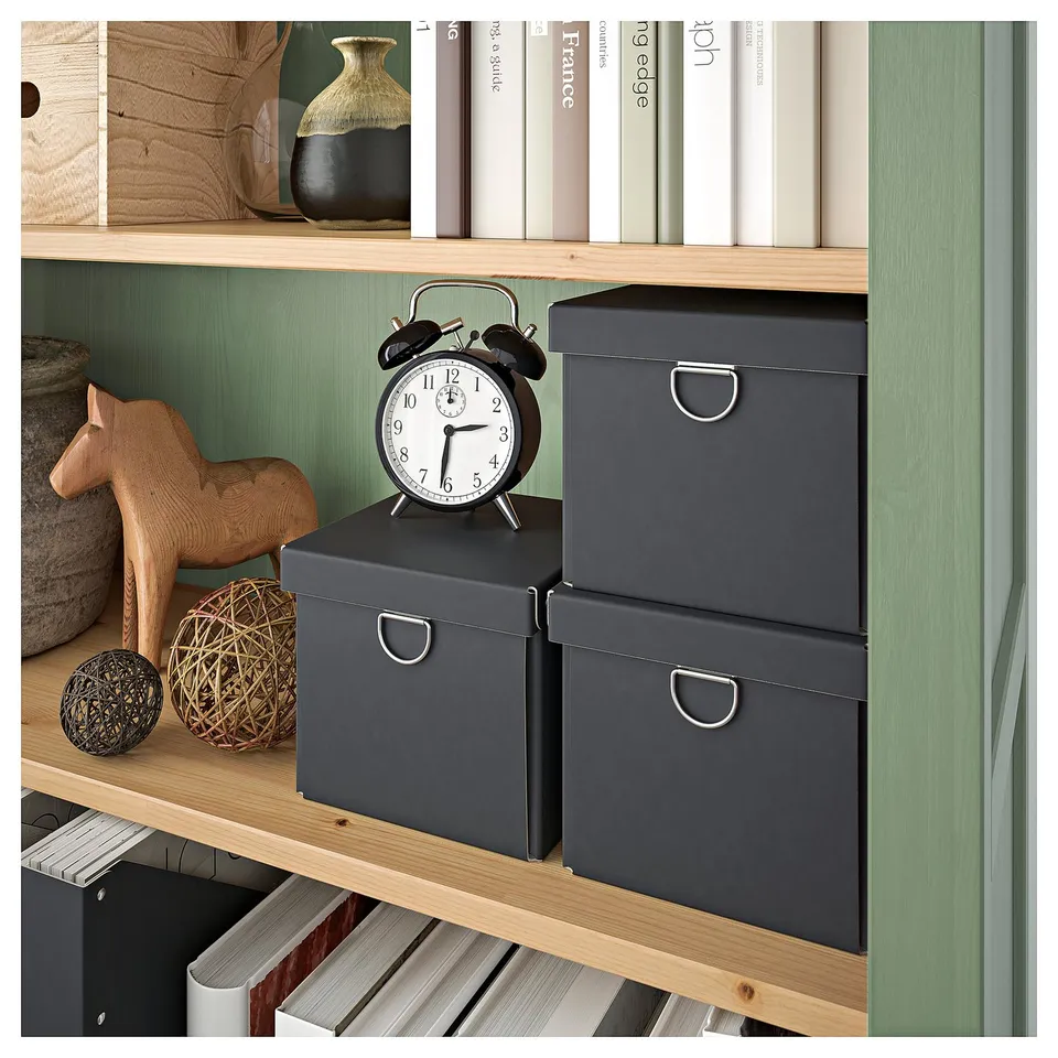 Green HEMNES bookshelf with boxes, clock, and decor. Wooden horse and metallic sphere on shelves.