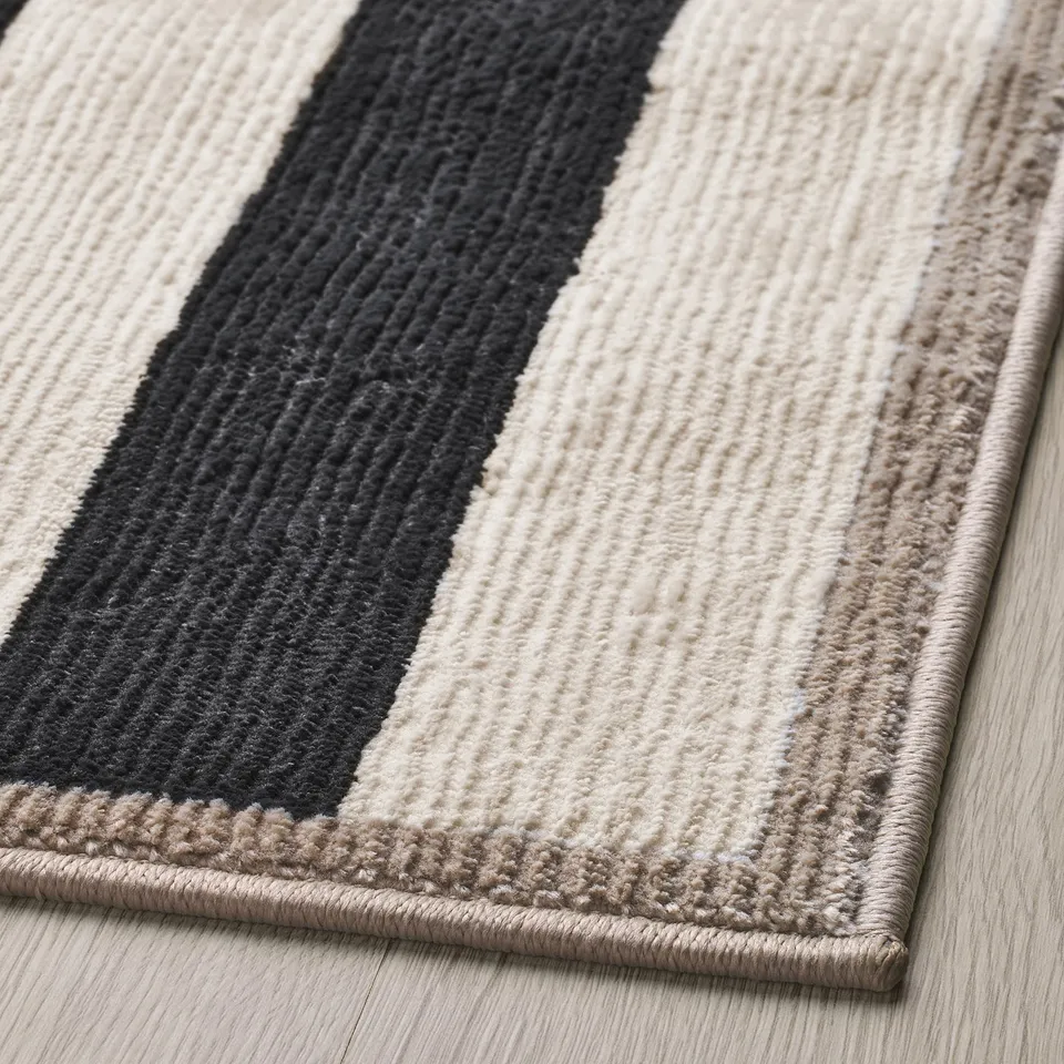 Modern horizontal striped rug with alternating black, tan, and white bands, featuring a soft texture and plush pile, situated on a wooden floor.