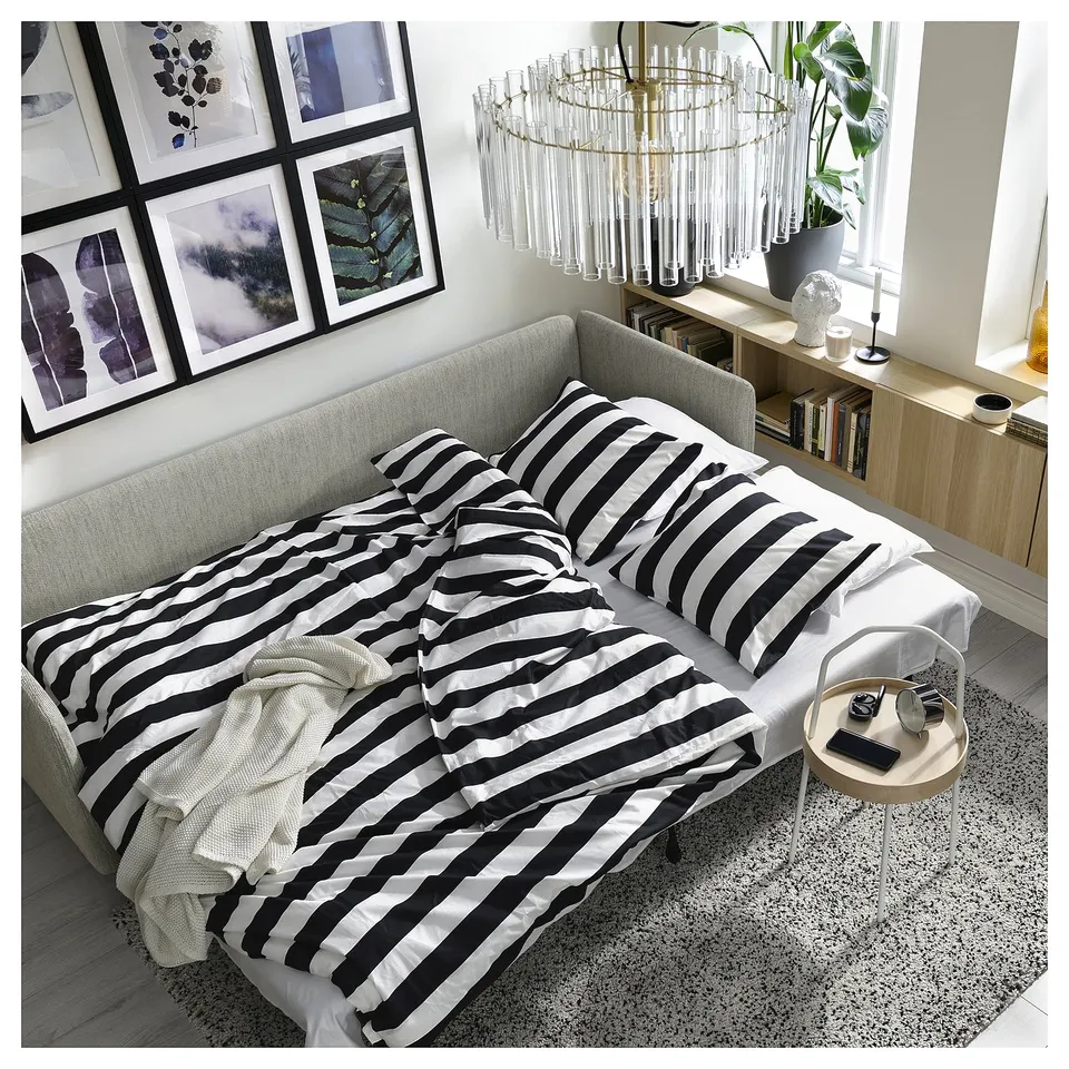 Modern living room with SÖDERHAMN grey sofa-bed, black-white striped bedding, cosy rug, stylish light fixture, and wall art.