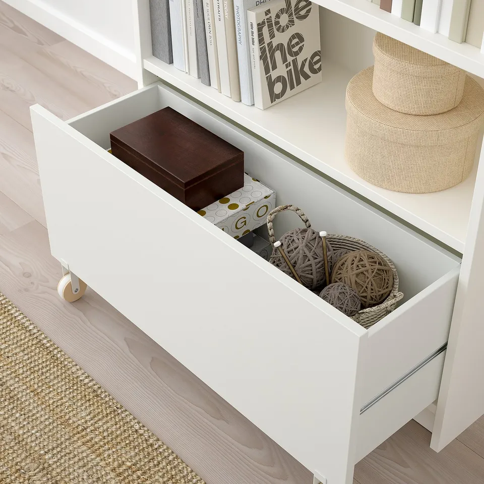 White BILLY bookcase drawer open showing storage bins and box, demonstrating hidden storage function.