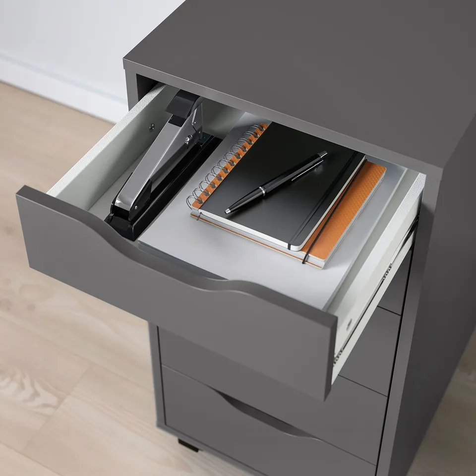 Open grey filing cabinet drawer with stapler, notebook, and pen.