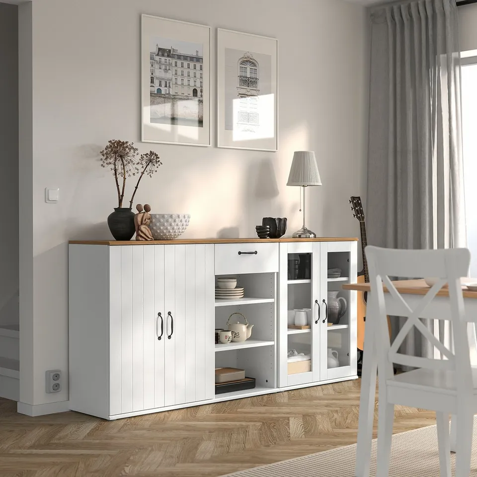 White cabinet with glass doors and plates inside, between wall and window.