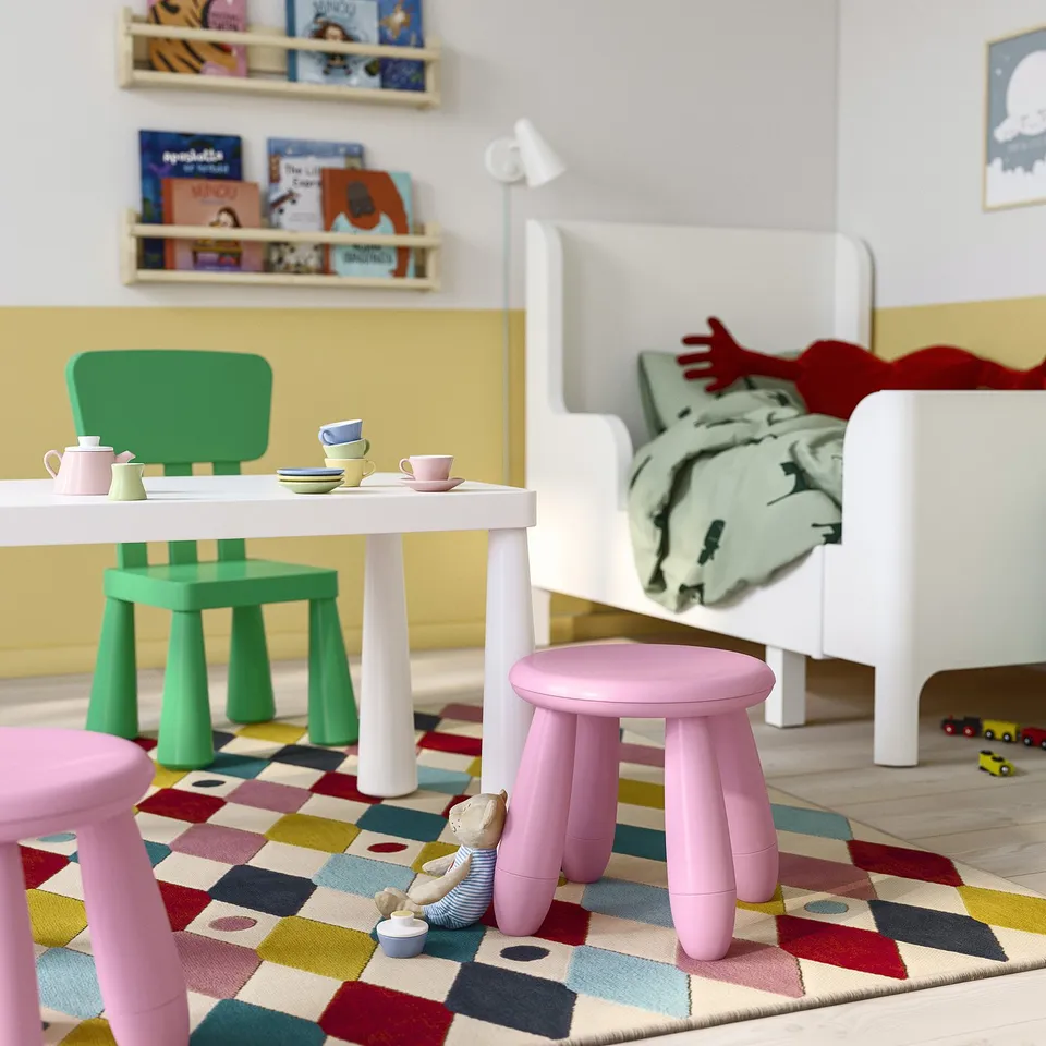 Playroom with MAMMUT table, green chairs, pink stools, toys, toddler bed, rug, bookshelves.