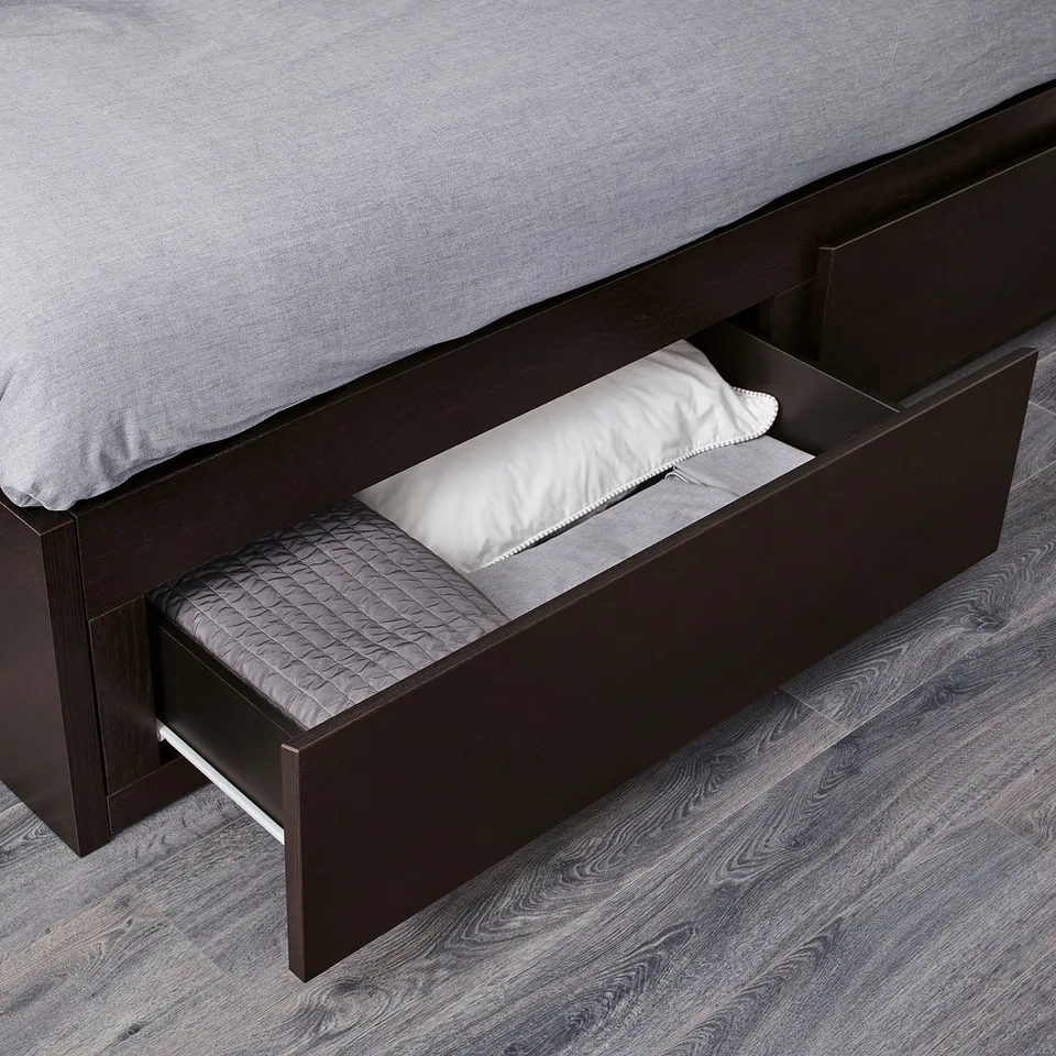 A dark wood daybed with a parked drawer for storage, containing linens.