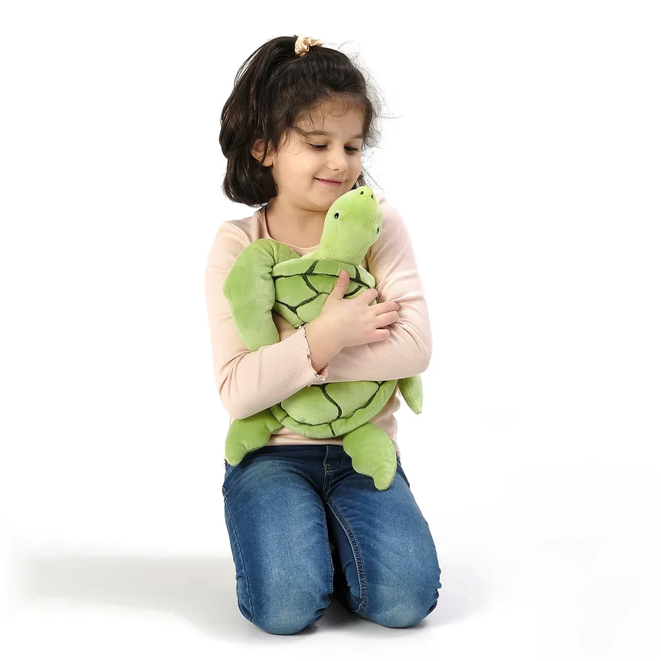 A child kneels hugging a soft green turtle toy, demonstrating its comfort and huggable nature.