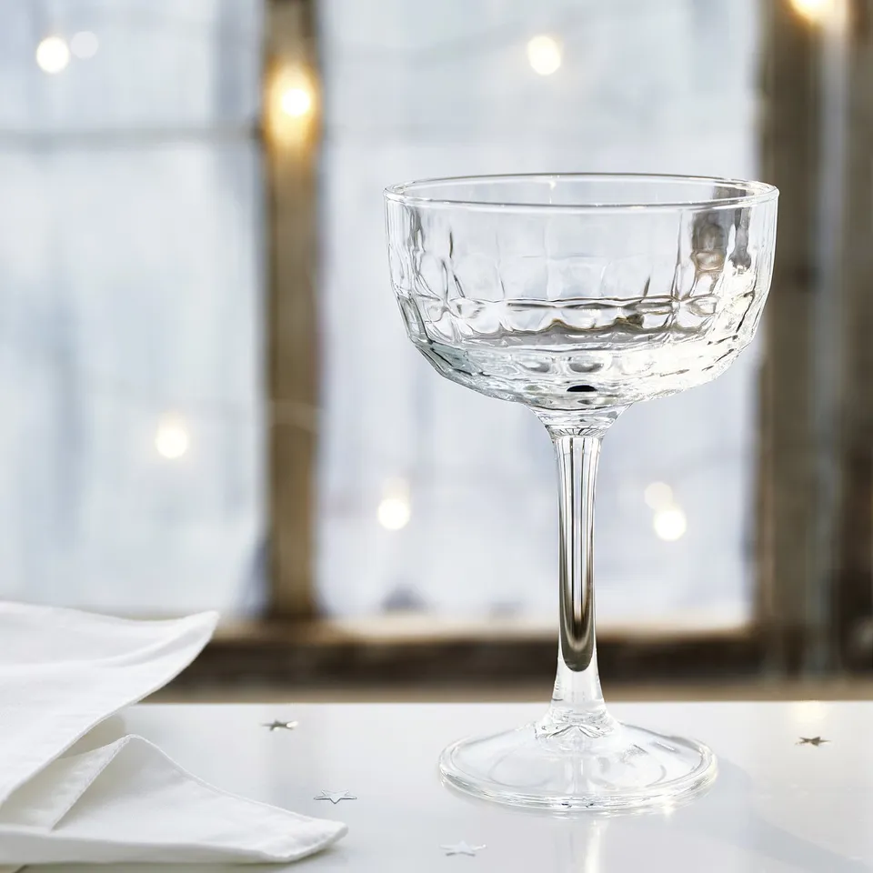 Elegant champagne coupe glass with intricate design sits on a pristine table.