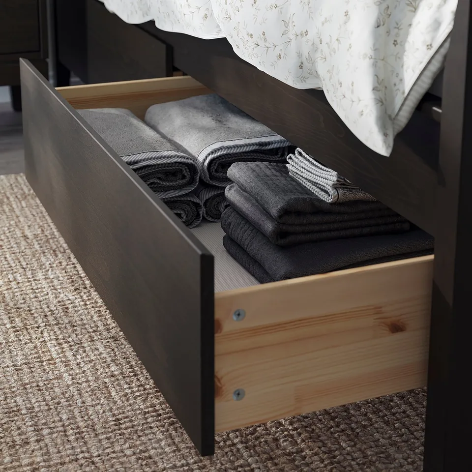 Open bedroom drawer shows neatly folded grey towels under a dark wood bed frame.