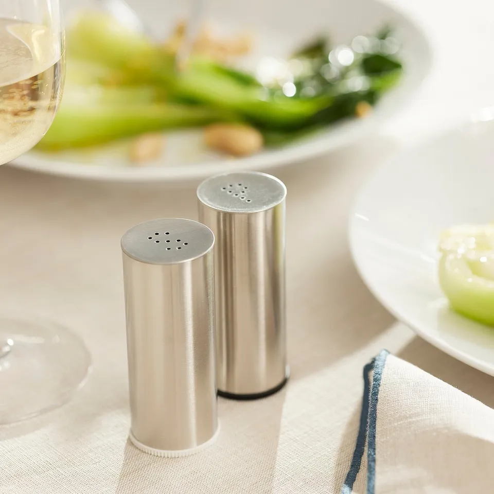 Metal salt and pepper shakers on a dining table near plates with food.