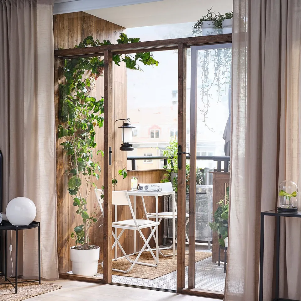 Modern bedroom with balcony & outdoor seating. Beige curtains frame glass door.