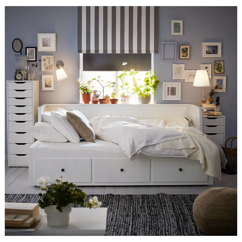 Bright, cosy bedroom with white HEMNES day-bed, striped curtains, and potted plants. Multiple framed artworks decorate the walls.