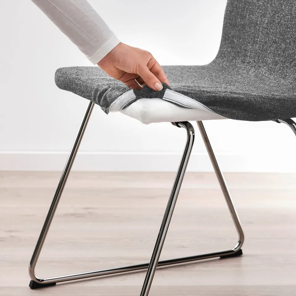 Person putting on a machine-washable seat cover on a modern upholstered chair with sled base.