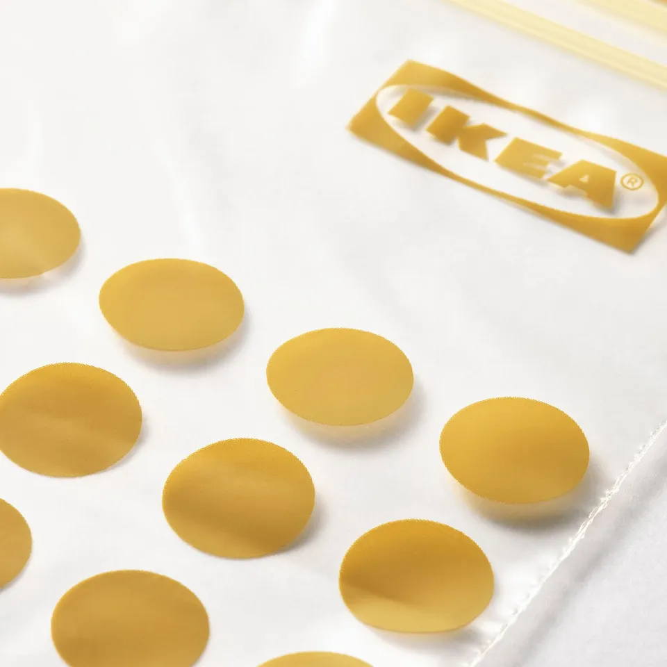 Multiple gold-colored, circular ikea ISTAD seals scattered on a white surface, with the ikea brand label visible in the background.