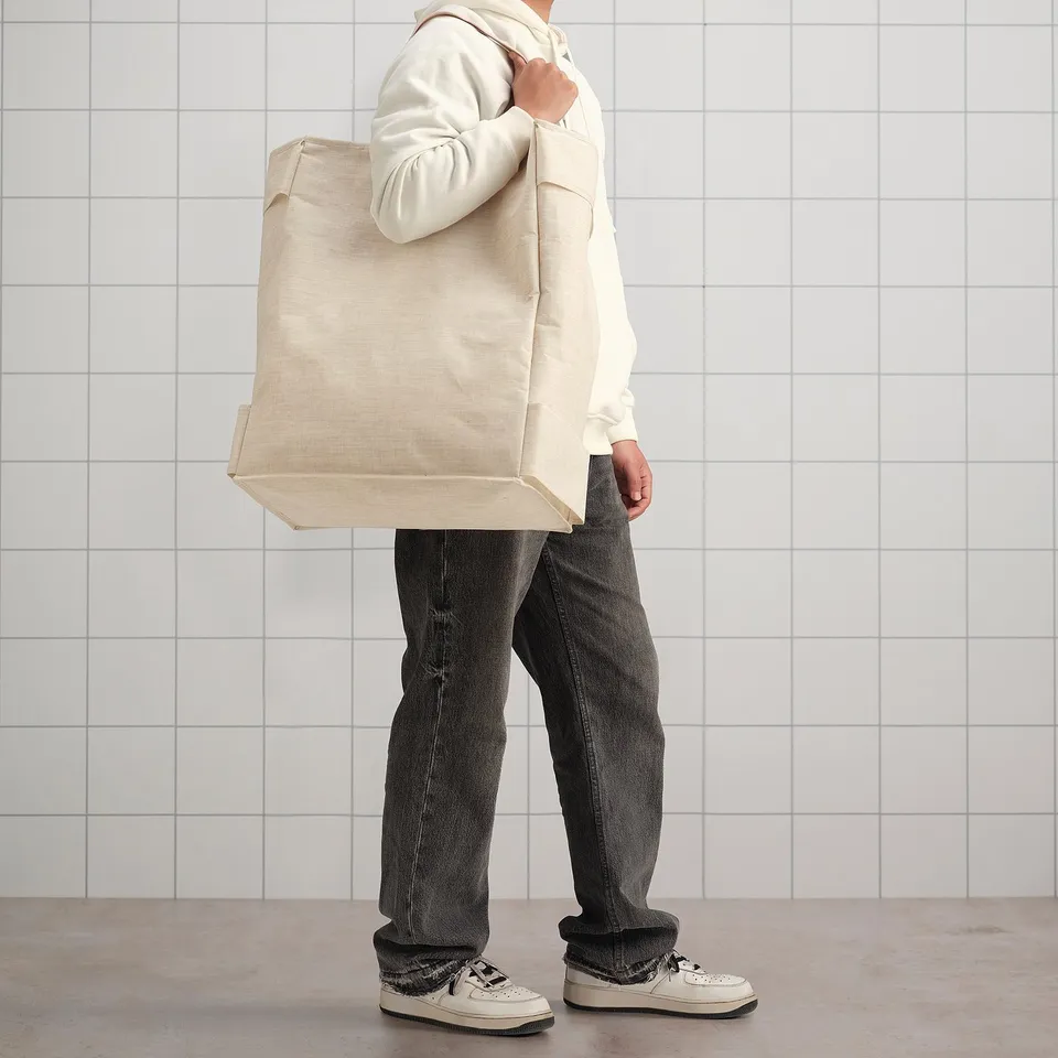 Person carrying large beige laundry bag, perfect for sorting whites and colours in narrow spaces.