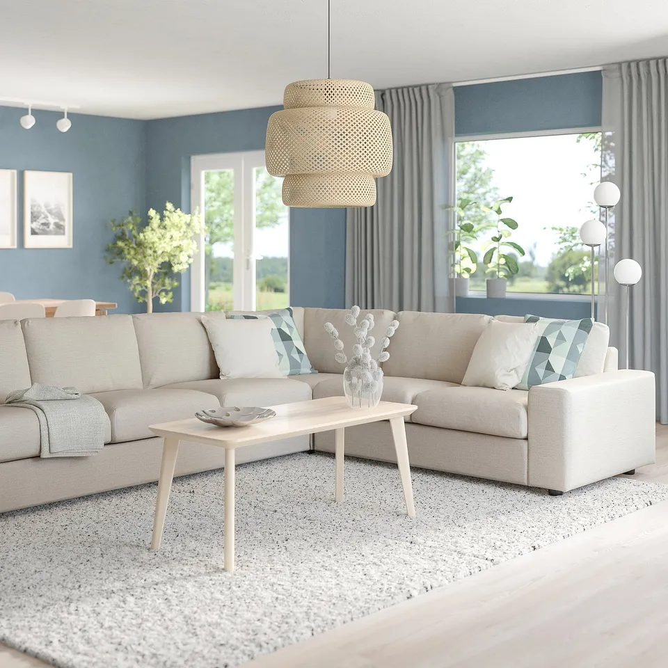 Modern living room with blue walls, large beige l-shaped VIMLE sofa, wooden coffee table, natural light, plants, and large window with curtains.