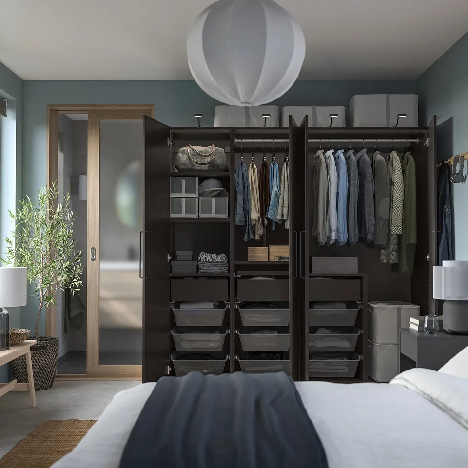 Modern bedroom with blue walls, black PAX wardrobe, clothes, and soft lighting.