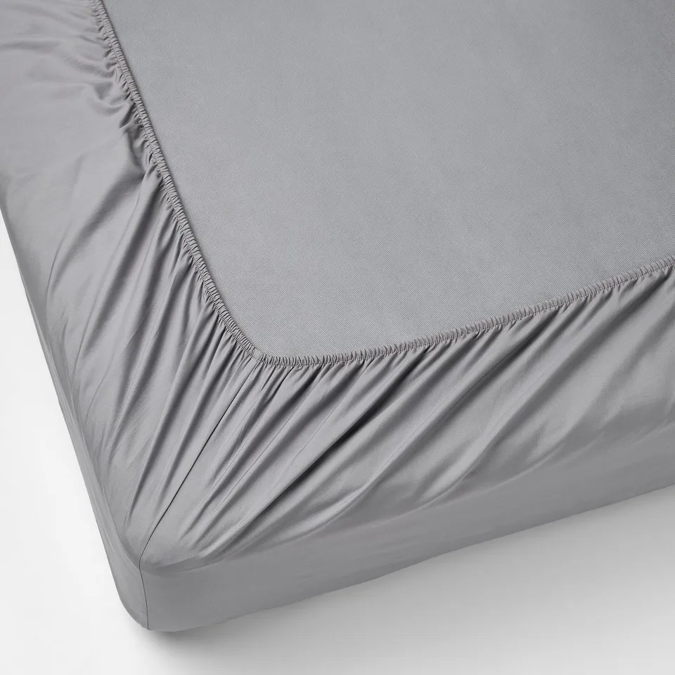 Grey fitted bed sheet with elastic edges covering a mattress corner.