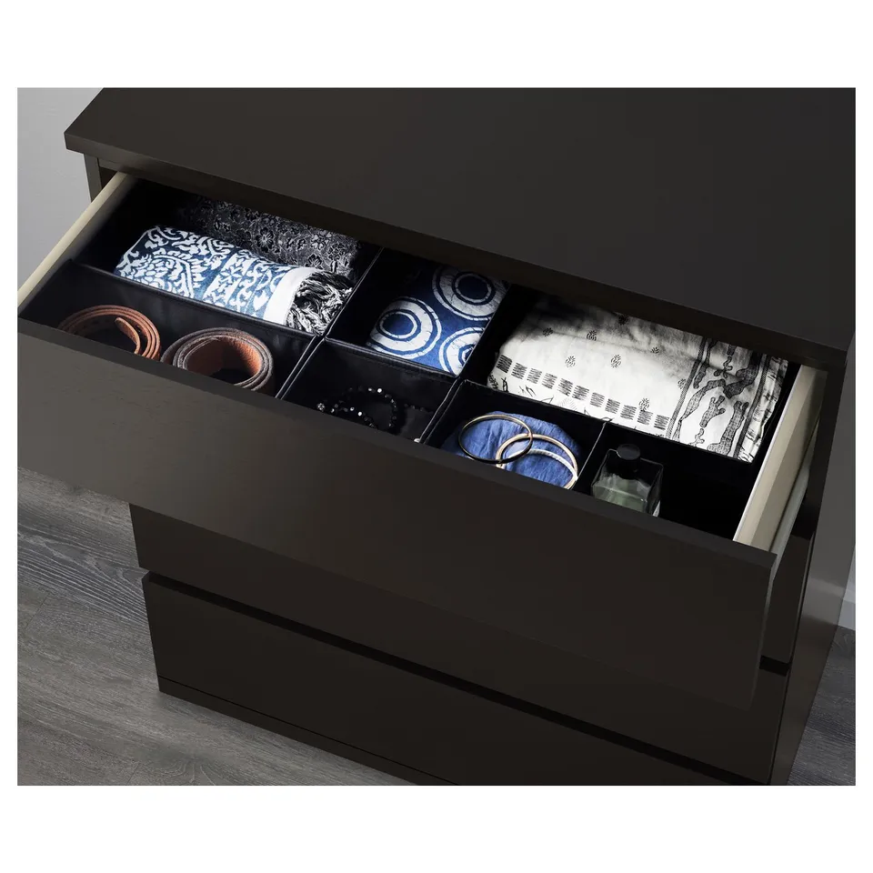 Black chest of drawers with open drawer, showing neat stacks of colourful clothes and accessories in compartments.