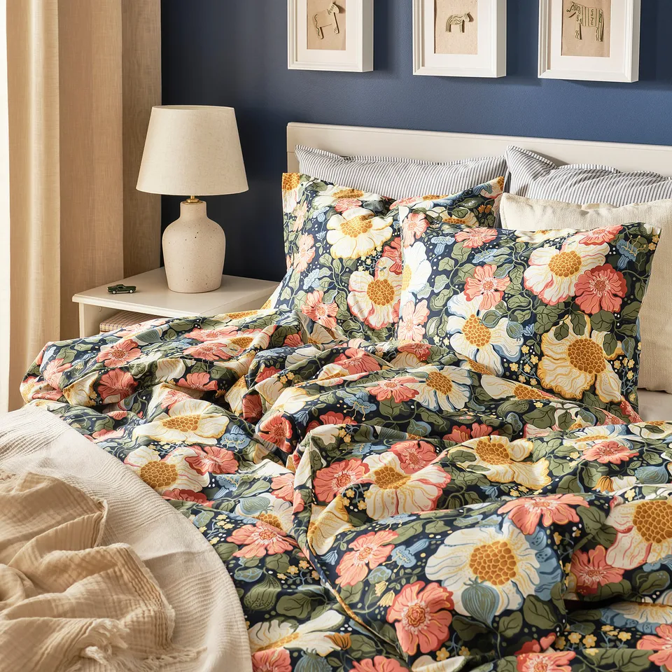 Dark blue floral duvet set with silky sateen-weave cotton/lyocell. Comfortable, inviting bed with pillows, lamp, and wall art for cosy ambiance.