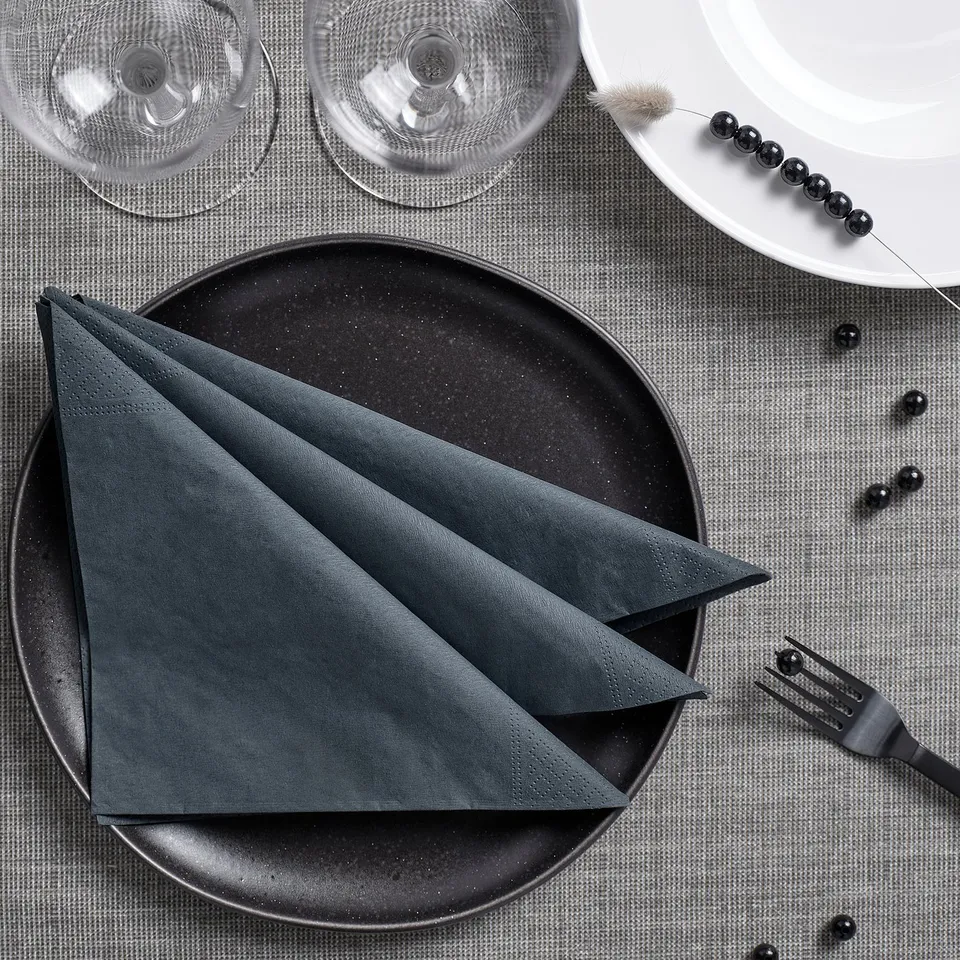 Table setting with dark grey napkins on black plate, white plate, wine glasses, silver fork.