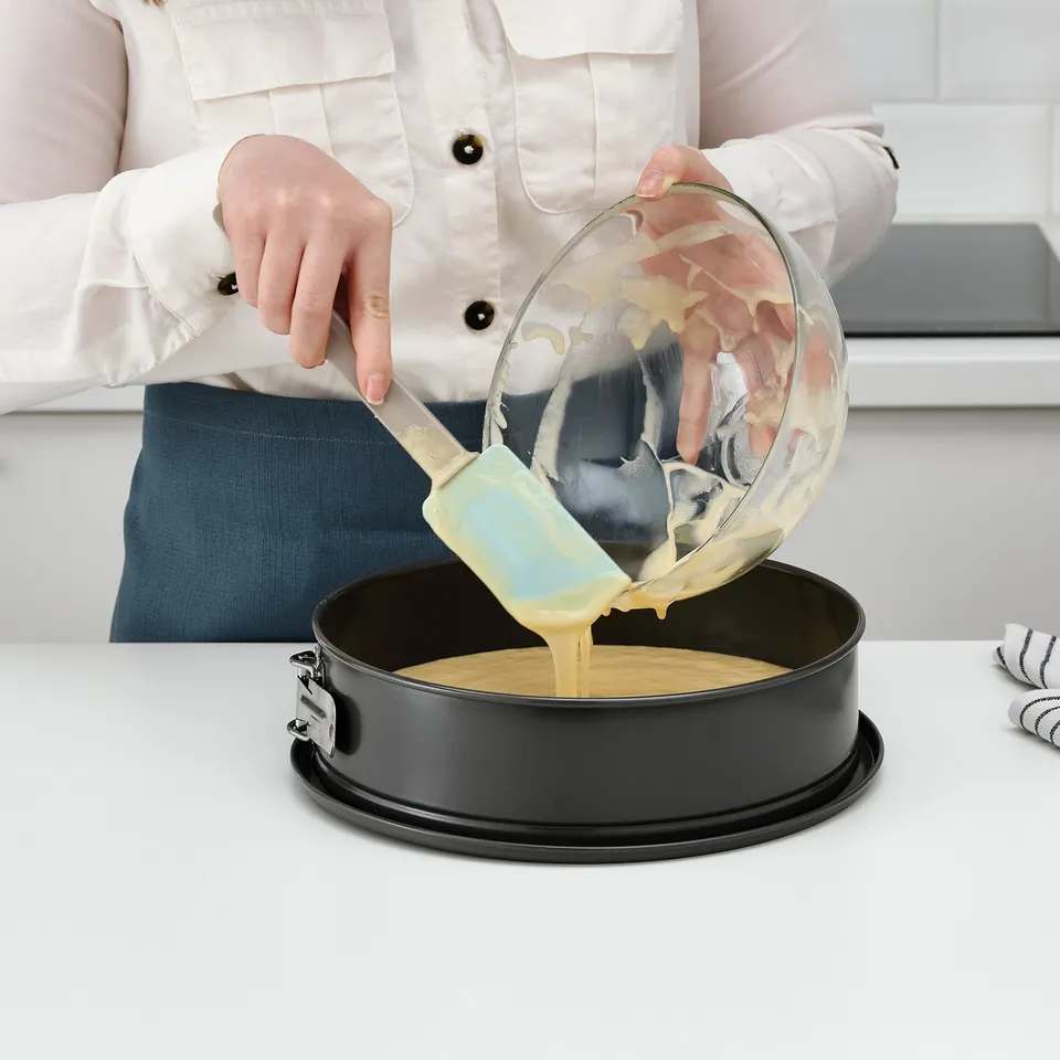A person pouring batter into a round cake pan on a clean countertop.