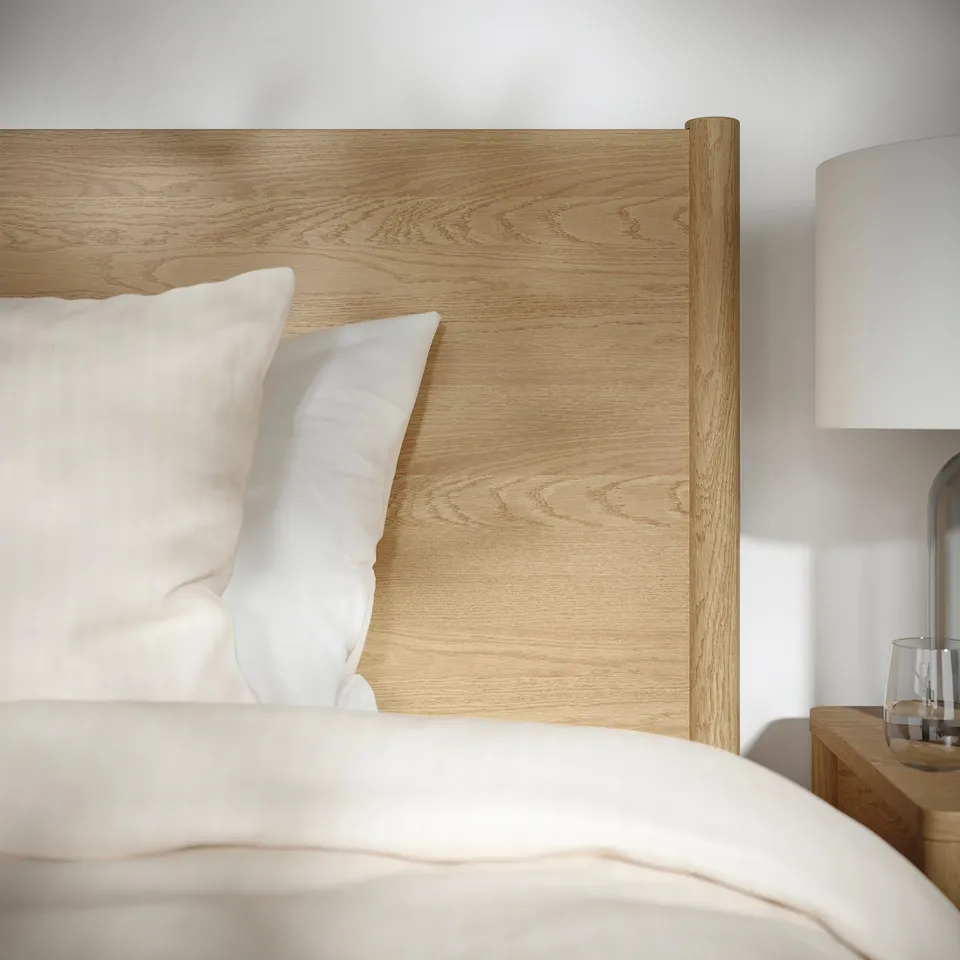 A modern bedroom featuring a wooden bed frame with light-colored bedding and a sleek lamp on a side table.