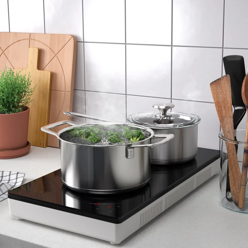 Kitchen counter with TILLREDA induction hob cooking broccoli, wooden utensils, and a plant.