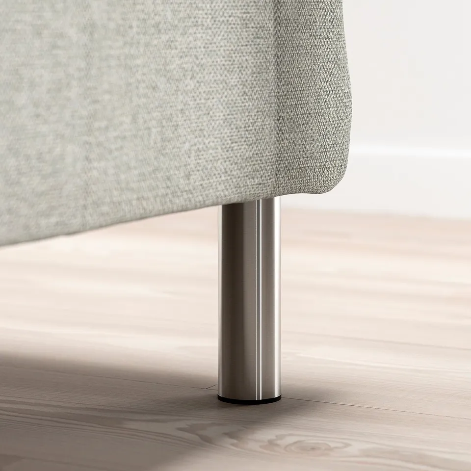Modern bed leg in silver metal for raised storage or robotic vacuum access.