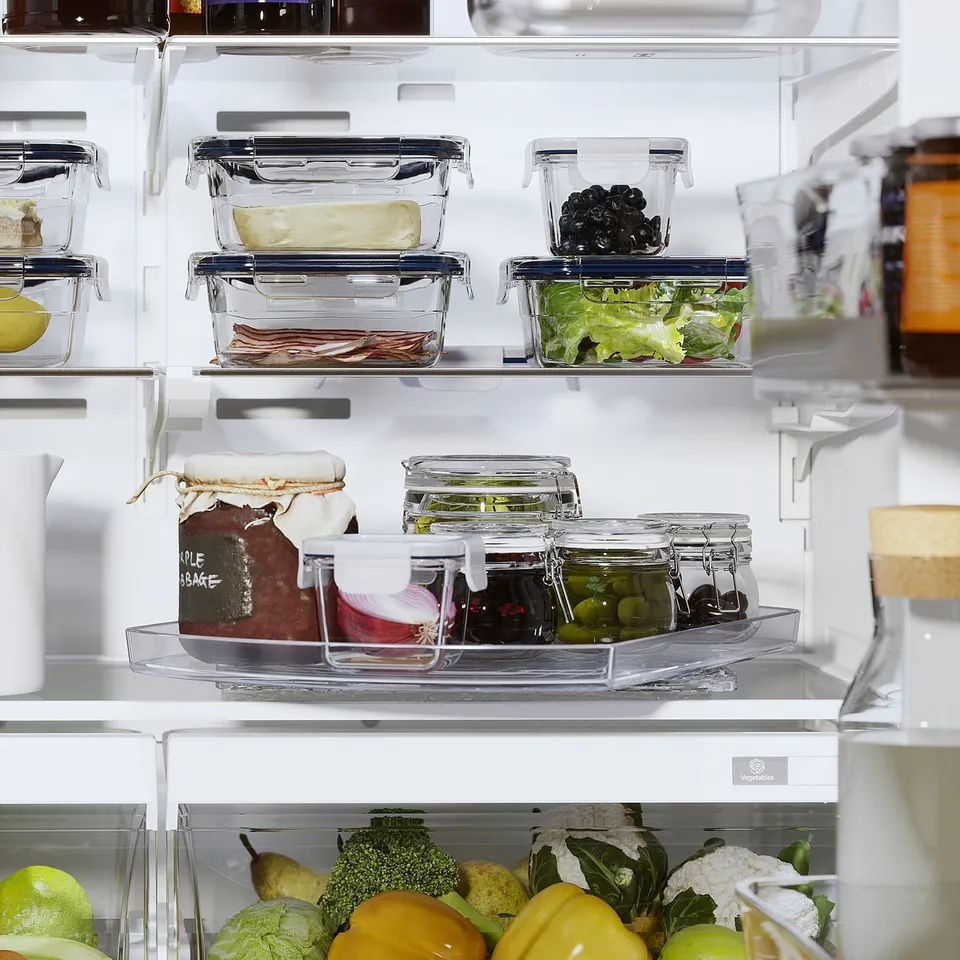 An organised refrigerator with white SNURRAD storage trays holding various fruits, vegetables, and glass containers of food.