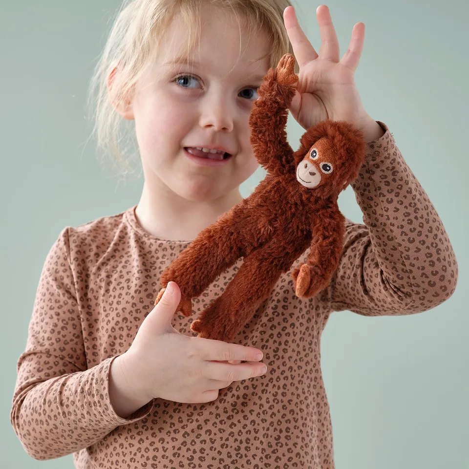 Blonde girl wearing leopard print shirt, happily holding plush orange monkey toy.