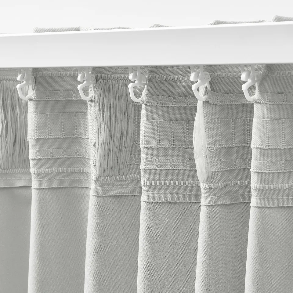 Close-up of grey KORGMOTT curtains, showing block-out fabric and multi-way hanging hooks.