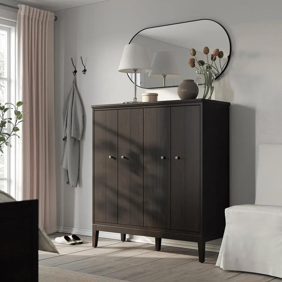 Modern entryway with IDANÄS dark-brown cabinet. Topped with mirror, lamp, and vase. Grey walls, pink curtains, hooks with coat.
