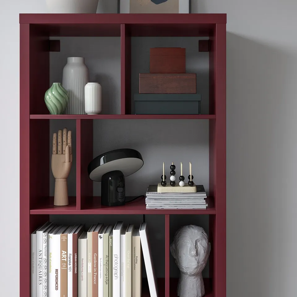 Red KALLAX shelf with art books, vases, wooden hand, speaker, candles, and bust.