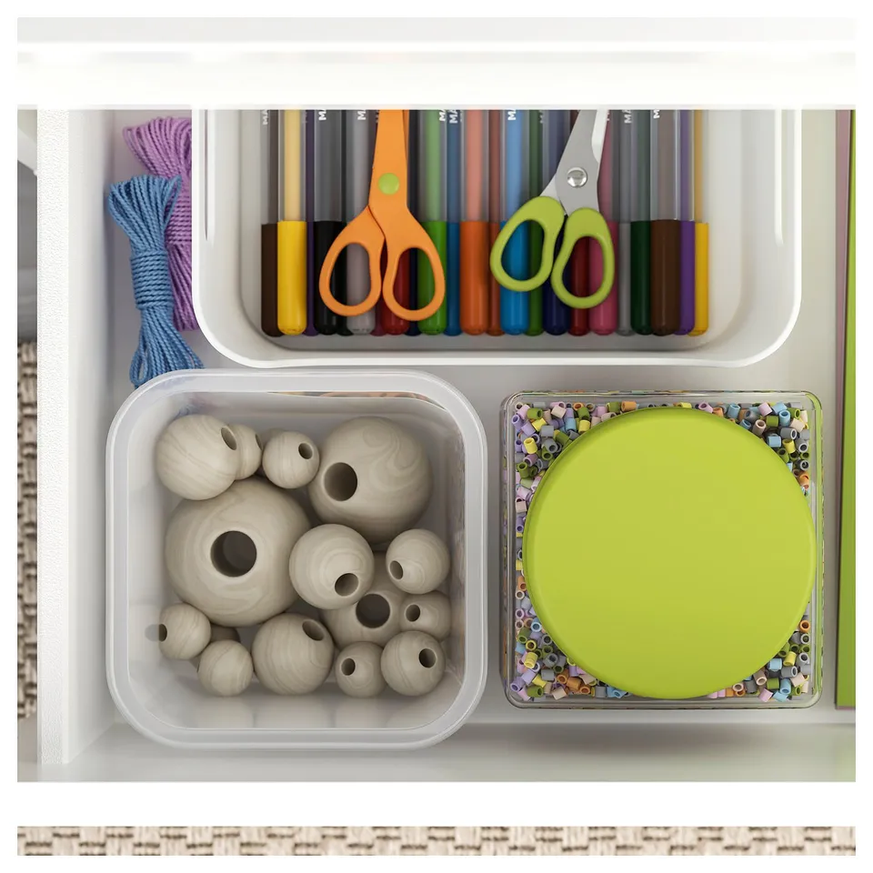 Organised drawer with crafts: coloured pens, scissors, yarn, wooden beads, and a lid in a white and green drawer set.