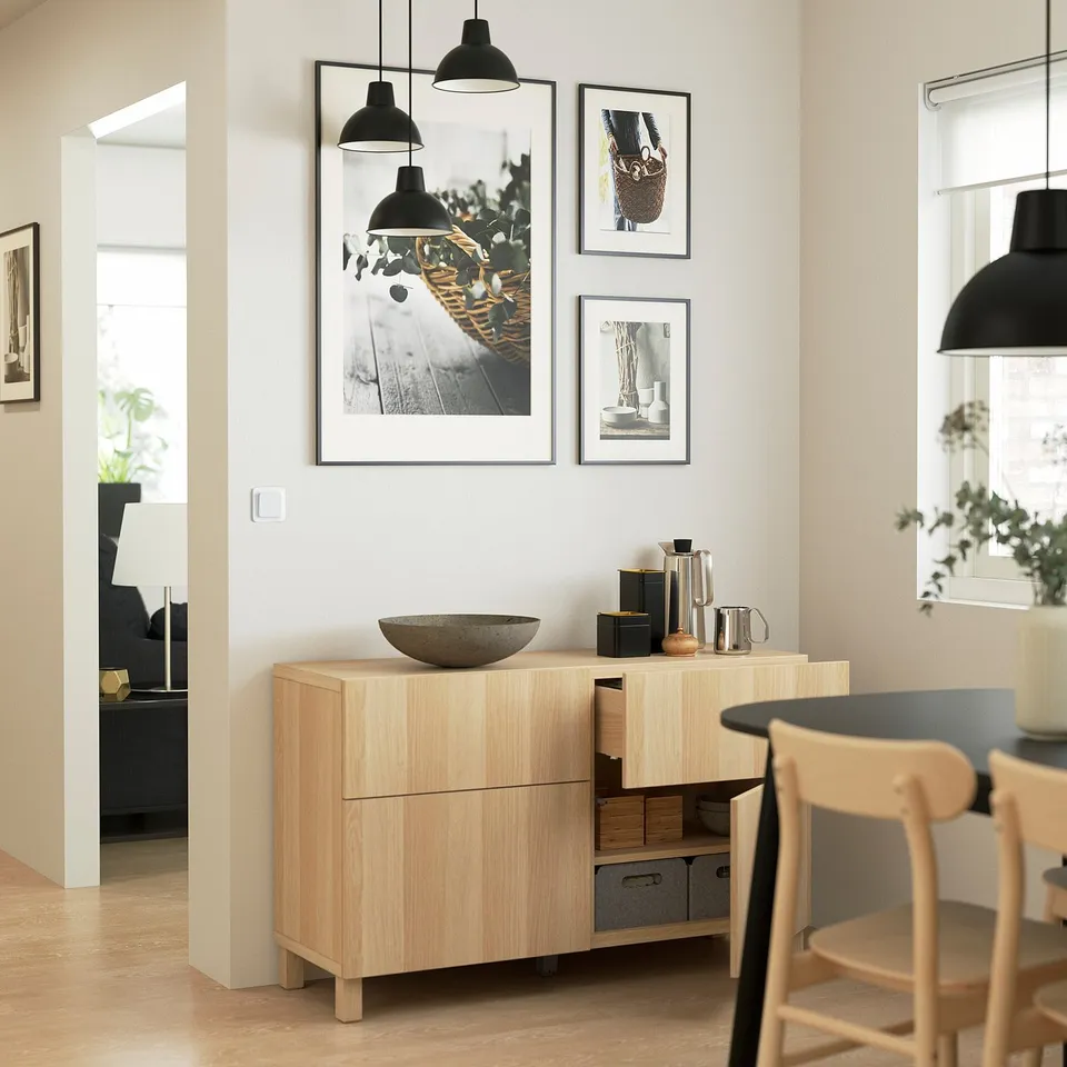 Modern dining room with light wood sideboard. Adjustable shelves, soft-closing drawers, and decorative bowl. Three framed pictures hang above.