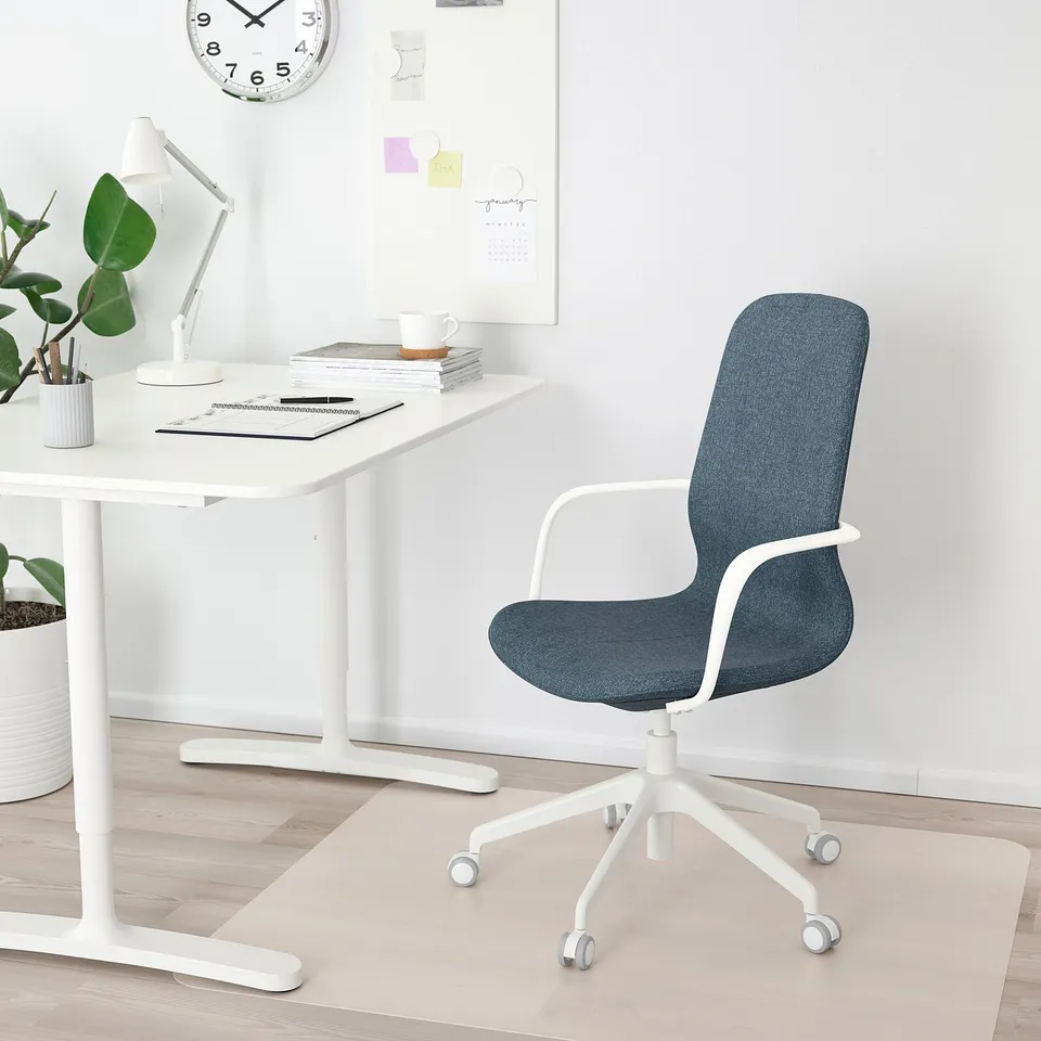 Modern minimalist home office. White desk, blue chair, white lamp, clock, plants, coffee cup, magazines.