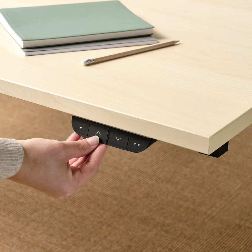 A person adjusts a motorised desks height using a control panel.
