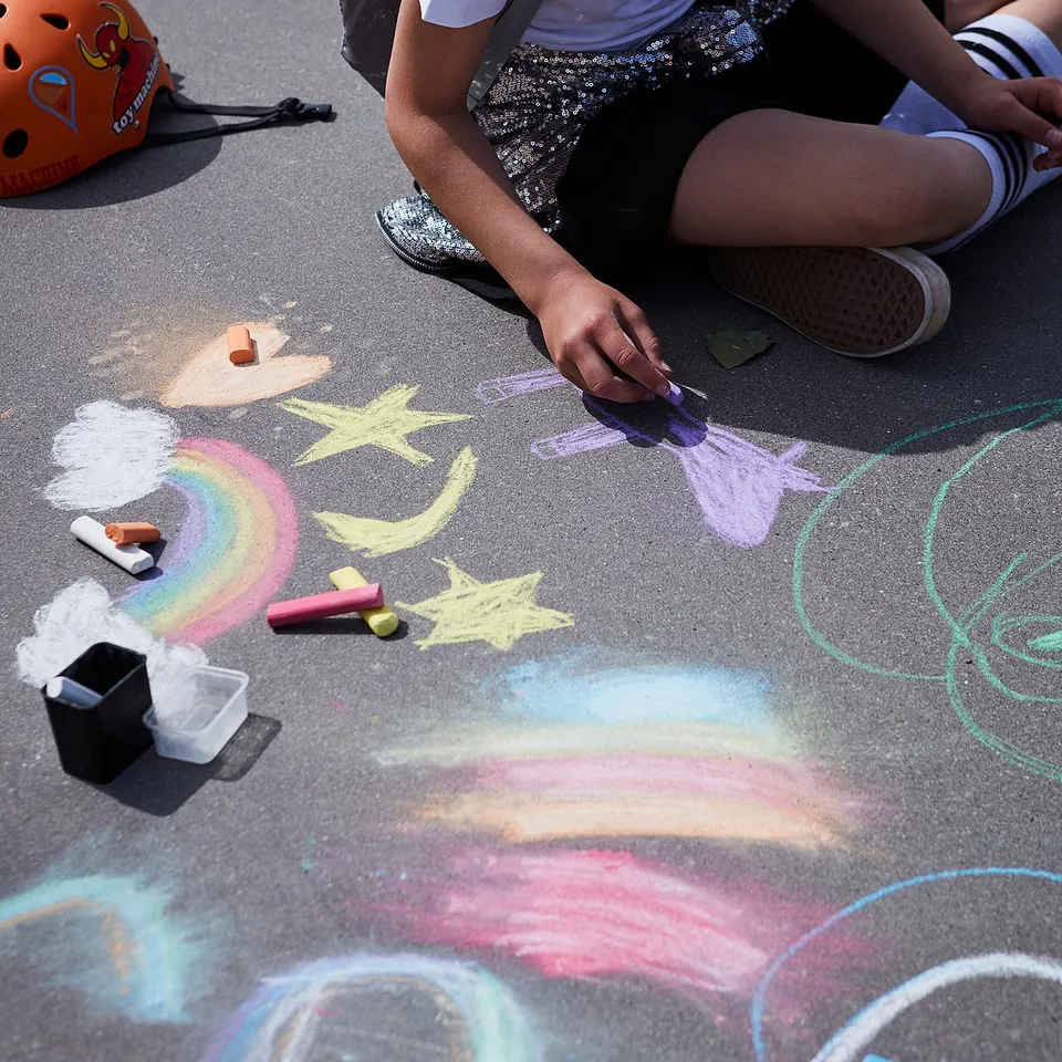 Girl in white skirt draws rainbows with chalk and helmet.