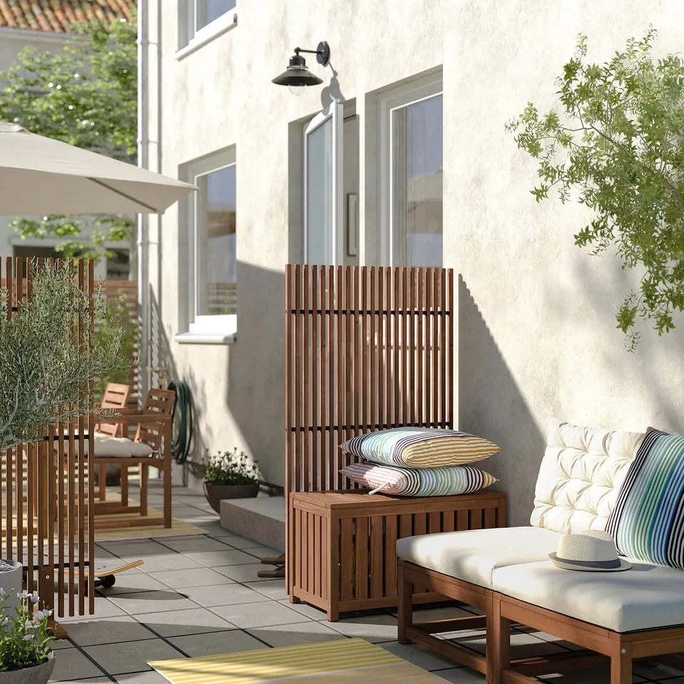 Outdoor patio with NÄMMARÖ wooden privacy screen, cushioned seat, and striped pillows, providing a cosy and private retreat.