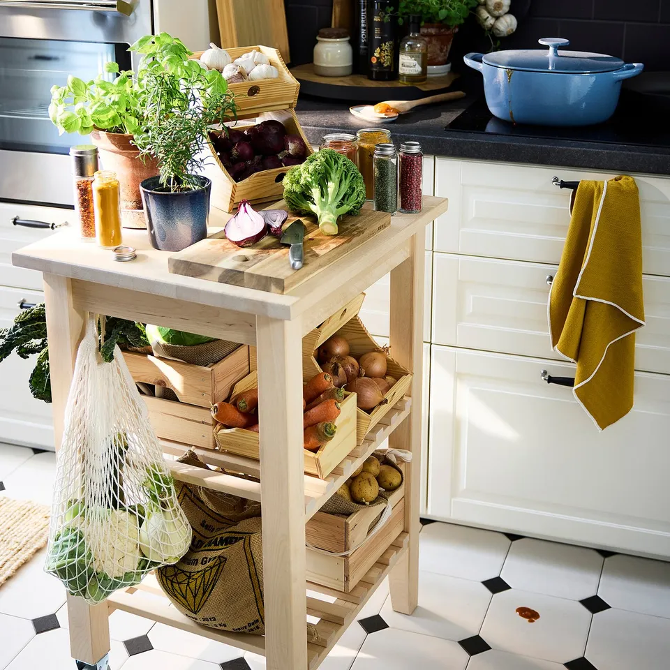 Kitchen island with wooden vegetable storage boxes on wheels, potted plants, herbs, and cooking supplies.