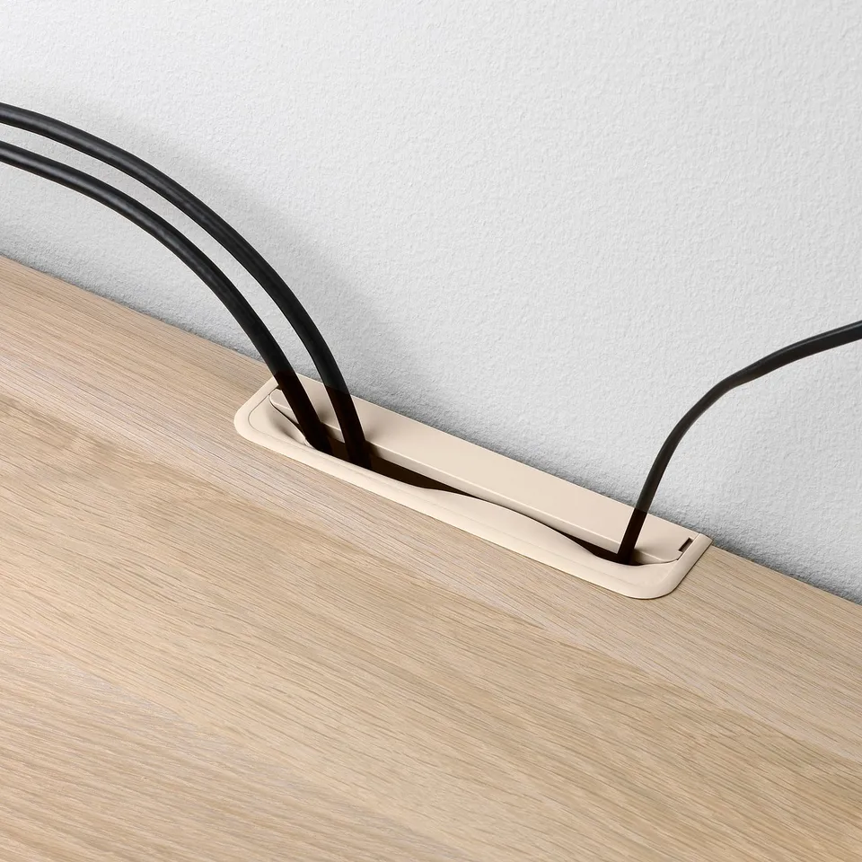 Cord management system: cables routed through a rectangular metal box into a wooden table, concealing wires for a tidy setup.