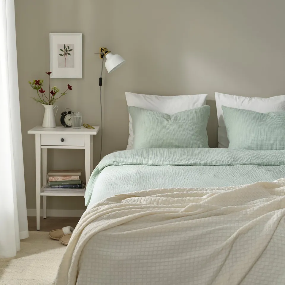 Bedroom with SCHERSMIN duvet, pillows, books, flowers, lamp, frame, and slippers.