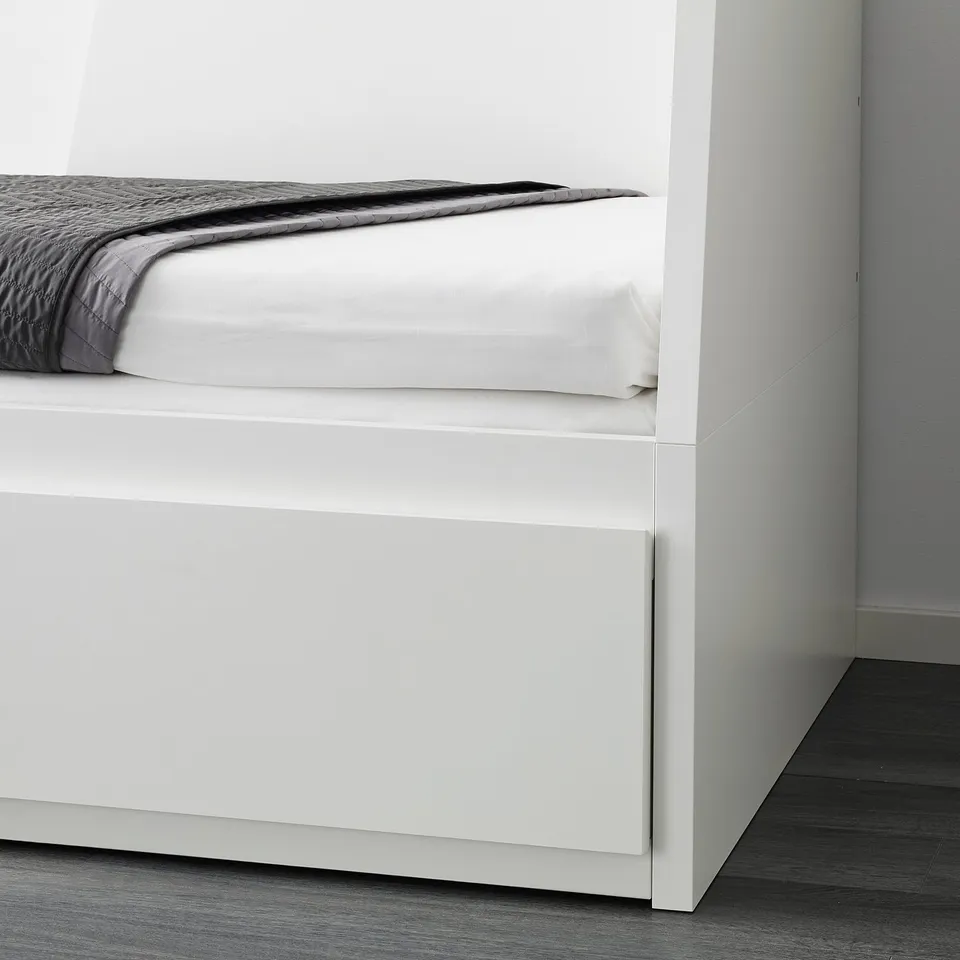 White day-bed with folded mattress and storage drawers. Part of foot visible.