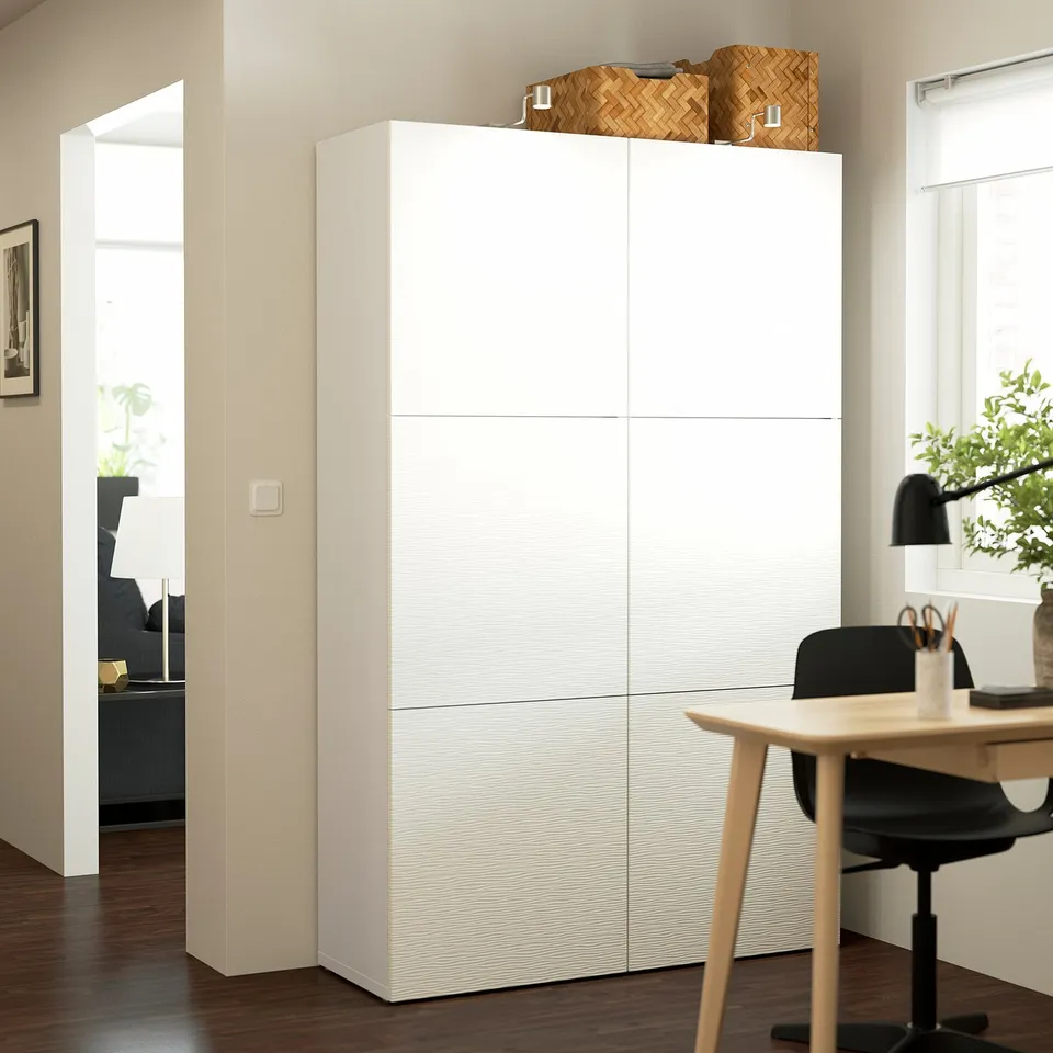 Modern room with white BESTÅ cabinet, tall & sleek, storing items on top, near a desk with chair.
