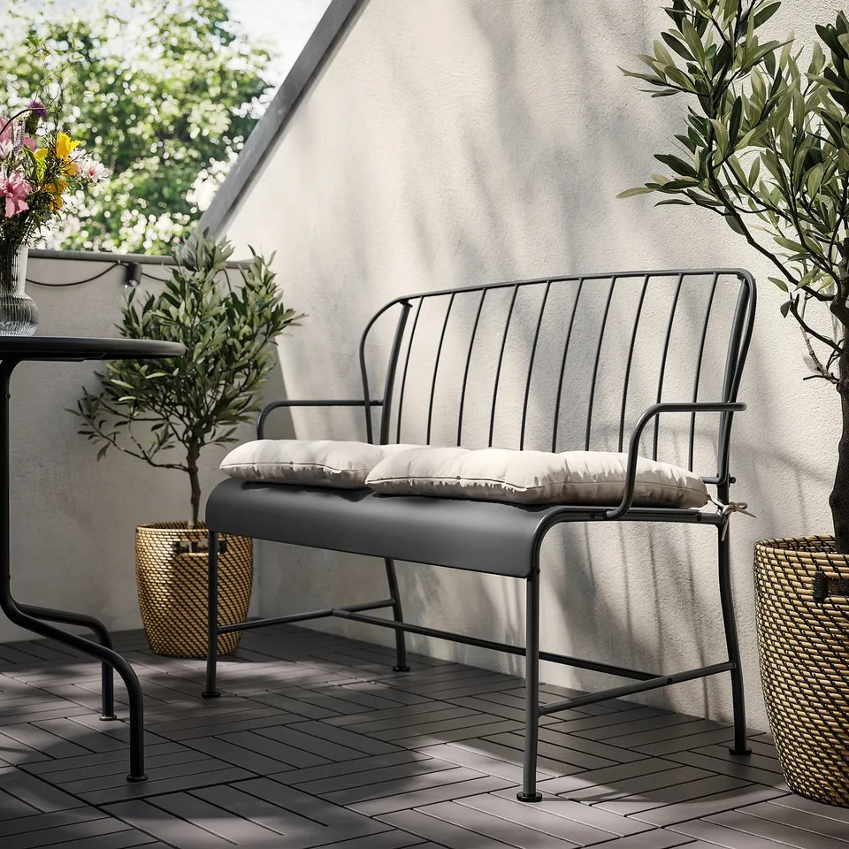 Modern black outdoor sofa with white cushions against a white wall. Sleek metal frame and comfortable seat padding.