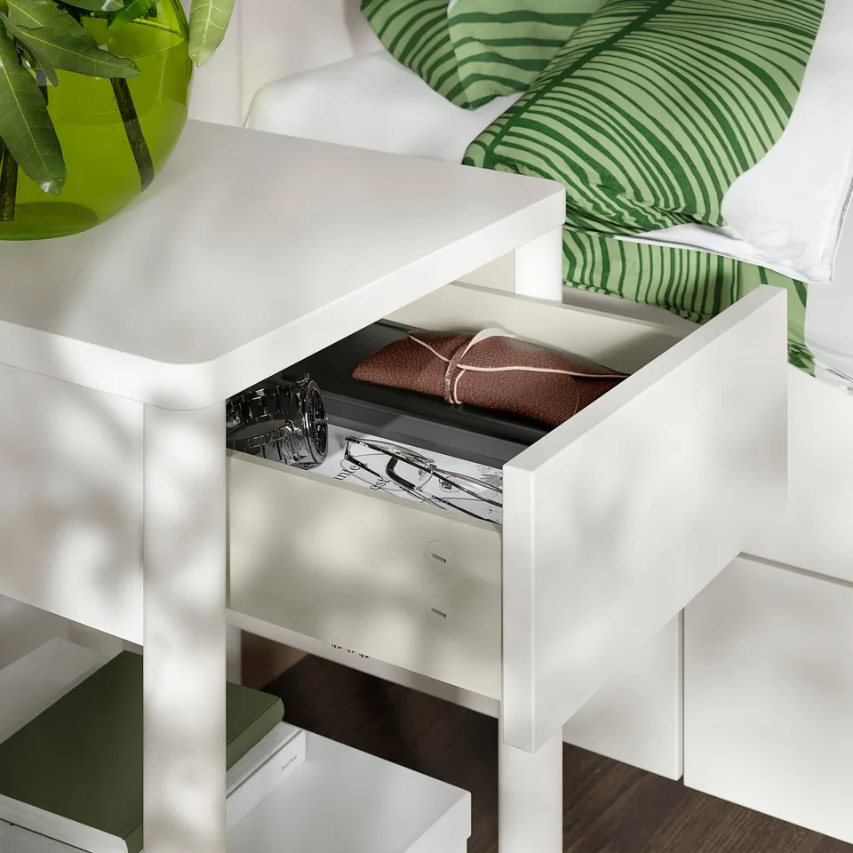 Open white drawer reveals stacked towels, beside striped green pillow.